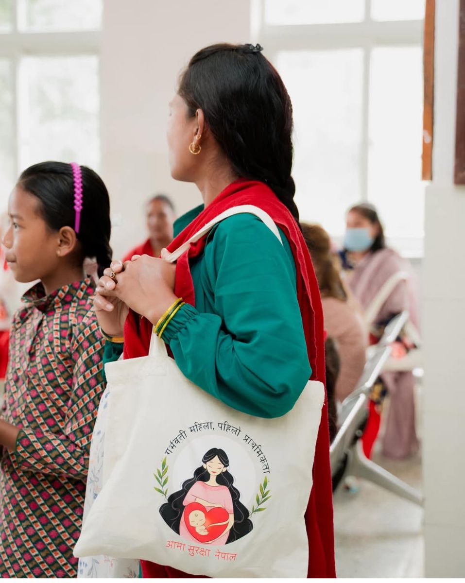A pregnant woman carrying an Aama Surakshya Nepal tote bag while waiting at a health service